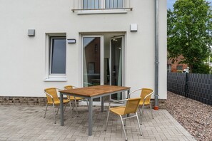 An outdoor patio with a table and four chairs, a sliding glass door, and a brick wall.