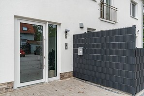A modern building with a white exterior, a black metal fence, and a glass door.