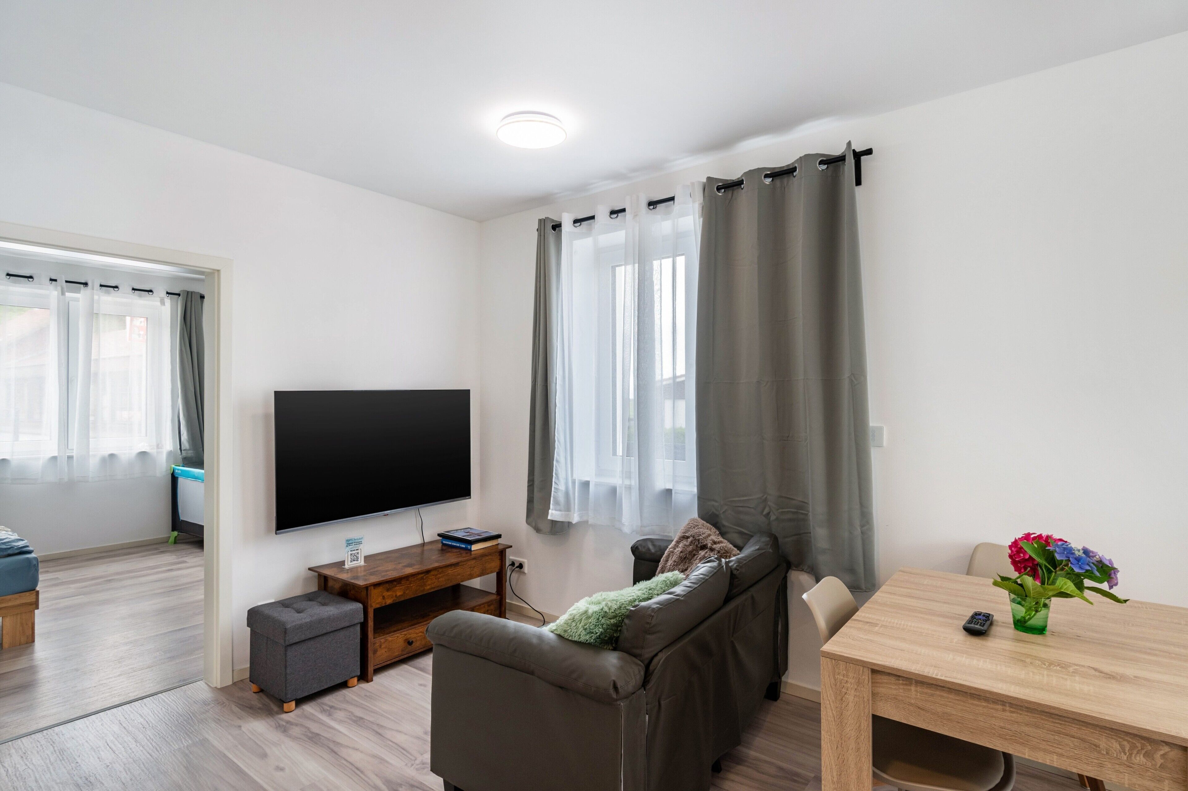 Ein modernes Wohnzimmer mit einem Flachbildfernseher, einem Sofa, einem kleinen Tisch und einem Esstisch.