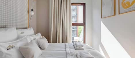 Ett hotellrum med en säng, kuddar, ett fönster, gardiner och konstverk på väggarna.