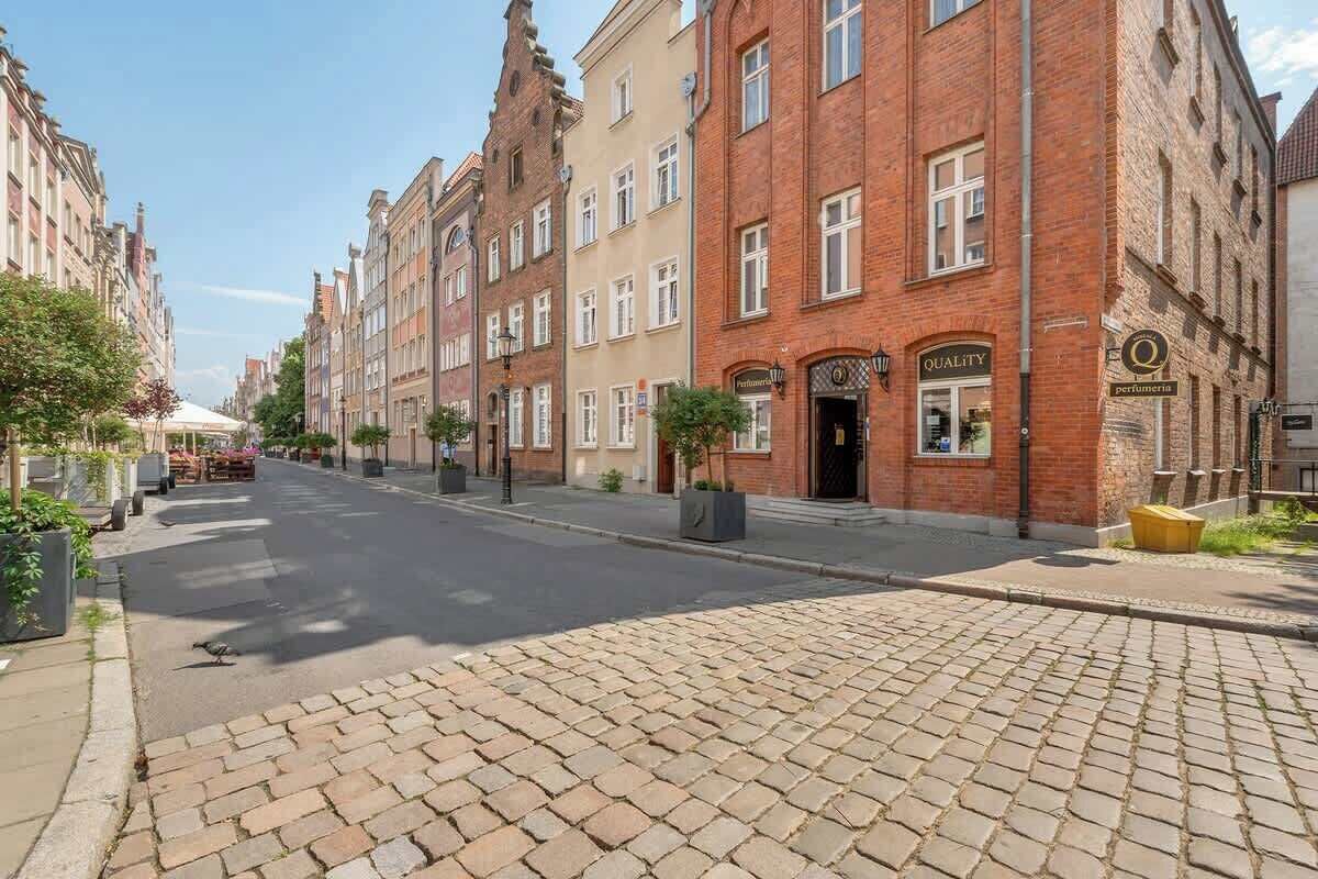 A cobblestone street lined with historic buildings, a clear sky, and a pedestrian walkway.