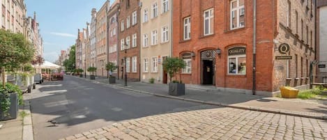 A cobblestone street lined with historic buildings, a clear sky, and a pedestrian walkway.