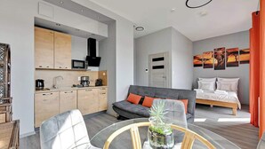 Ett kompakt bostadsutrymme med ett litet kök, en matplats, en soffa, en säng och en vägg med konstverk.
