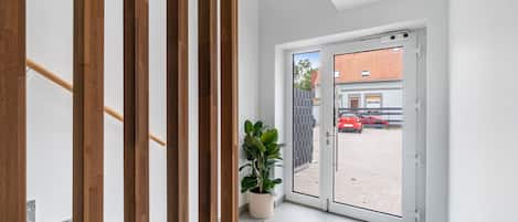 A modern interior with a wooden staircase, a potted plant, and a view of a red car outside through a glass door.