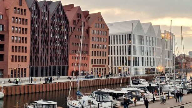 En småbåtshamn med förtöjda båtar, en strandpromenad och byggnader med tydliga och särpräglade arkitektoniska stilar.