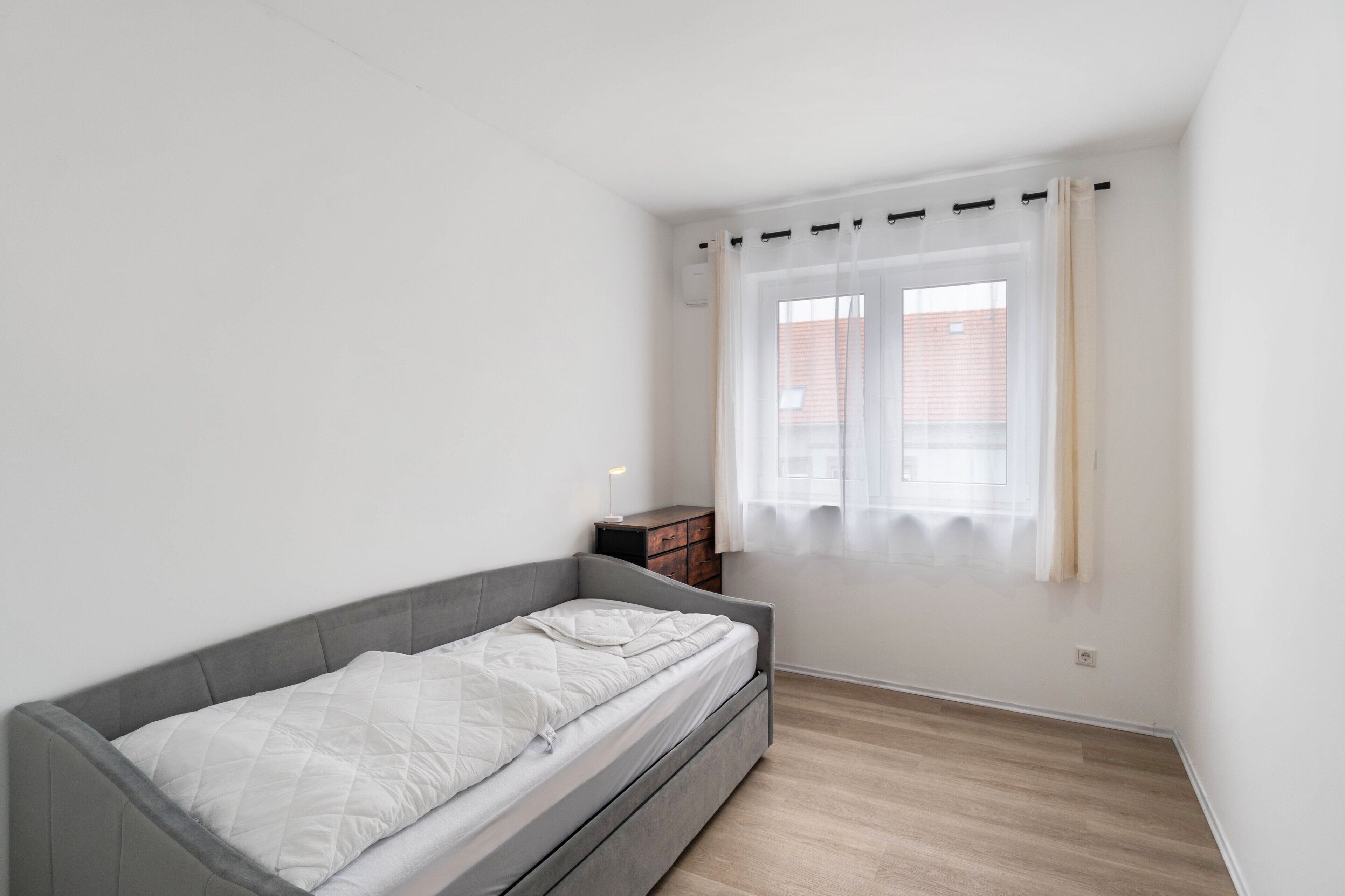 A minimalist bedroom with a single bed, a bedside table, and a window with curtains.