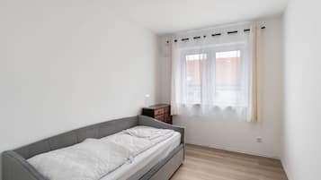 Un dormitorio minimalista con una cama individual, una mesita de noche y una ventana con cortinas.
