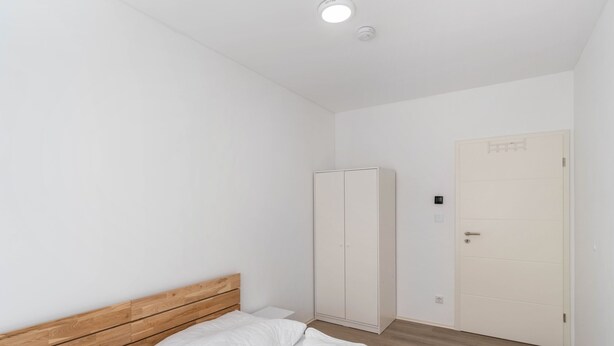 A bedroom with a wooden headboard, a bed with white bedding, a wardrobe, and a door with a handle.