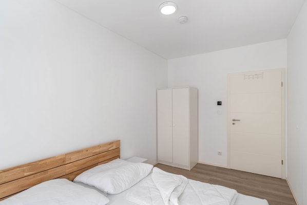 A bedroom with a wooden headboard, a bed with white bedding, a wardrobe, and a door with a handle.