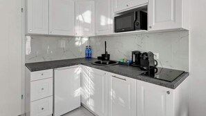 A modern kitchen with white cabinets, a black countertop, a microwave, and a coffee maker. - Długa Street | Main Old Town (Gdańsk)