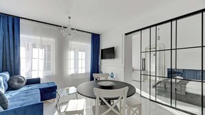 A modern living room with a sofa, dining table, chairs, a TV, and a large glass partition. - Długa Street | Main Old Town (Gdańsk)