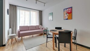 Ein modernes Wohnzimmer mit einem rosafarbenen Sofa, einem Esstisch mit Stühlen, einem Heizkörper und einem Fenster mit Vorhängen.