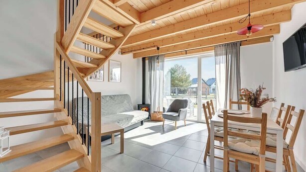 Et moderne interiør med en trappe i træ, en sofa, et spisebord med stole og en pejs.
