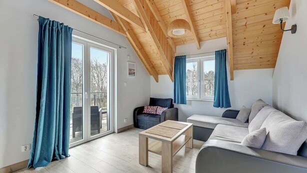 A modern interior with a wooden ceiling, a sofa, a table, and a view through a glass door. - Dębki 5 | Rodzinny Apartament | Nad Morzem (Dębki)