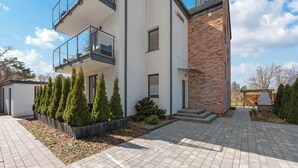 A modern two-story house with a balcony, a brick section, and a paved driveway. - Dębki 5 | Rodzinny Apartament | Nad Morzem (Dębki)