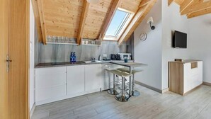 A modern kitchen with wooden beams, a skylight, bar stools, a microwave, and a TV. - Dębki 5 | Rodzinny Apartament | Nad Morzem (Dębki)