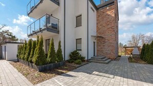 Un edificio moderno de dos pisos con balcón, sección de ladrillo y entrada pavimentada.