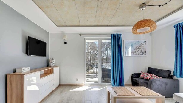 Una sala de estar moderna con televisor, muebles de madera, un sofá y un amplio ventanal con cortinas.