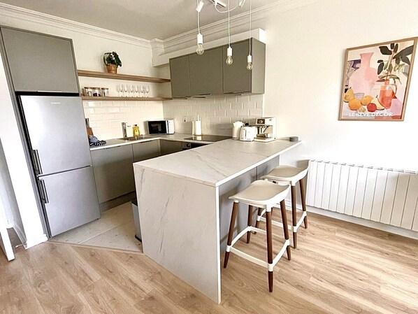 A modern kitchen with a central island, bar stools, a microwave, and a coffee machine.