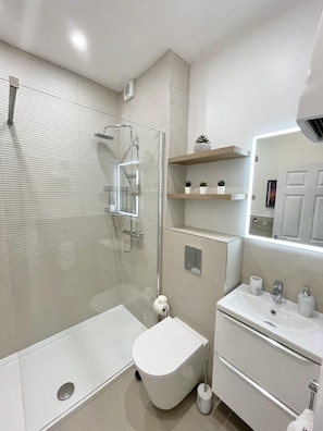 Un baño moderno con ducha de vidrio, inodoro, lavamanos y espejo.
