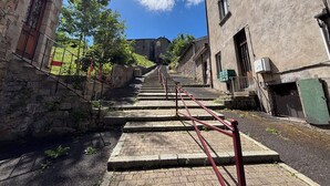 Un estrecho callejón con edificios de piedra, una escalera y un cielo azul despejado.