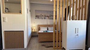 Un dormitorio con una cama de madera, un armario blanco, un radiador, un espejo instalado en la pared y un cuadro.