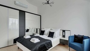 Una habitación de hotel moderna con una cama, un sillón azul, un espejo grande y un aplique de techo.