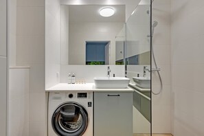 Ein modernes Badezimmer mit Waschmaschine, Waschbecken und Dusche.