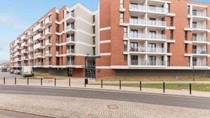 A multi-story residential building with balconies, a gated entrance, and a paved sidewalk. - Aura IV 25 | City Center | near Gdansk Shipyard (Gdańsk)