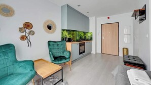 A modern living room with a sofa, a small table, a kitchen area with a stove, and a door. - Aura IV 25 | City Center | near Gdansk Shipyard (Gdańsk)