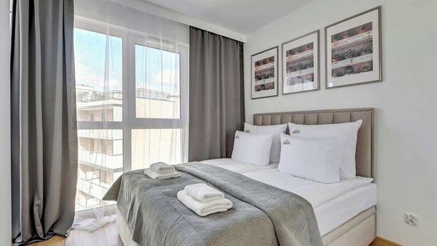 Ett hotellrum med en säng, gardiner och tre inramade tavlor på v äggen.