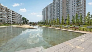 Ett bostadskomplex med en central pool, omgivet av grönska och bänkar.