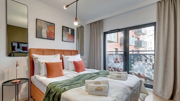 Quarto de hotel com cama, mesa de cabeceira, luminária, janela com vista e obras de arte na parede.