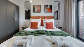 Quarto de hotel com uma cama, duas mesinhas de cabeceira, uma janela grande e obras de arte na parede.