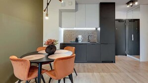 Uma cozinha moderna com ilha central, armários escuros e um espaço de refeições com cadeiras laranja e uma mesa redonda.