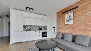 Een moderne keuken met witte kastjes, een betegelde achterwand en een zithoek met een grijze bank en een ronde tafel.