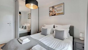 Ein modernes Hotelzimmer mit einem großen Bett, einem Nachttisch mit Lampe, einem Spiegel und einem gerahmten Bild an der Wand.