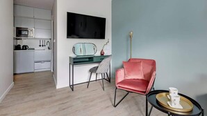 Et moderne opholdsrum med et køkken, et skrivebord, en rød stol og et fladskærms-tv.
