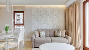Ein modernes Wohnzimmer mit einem beigefarbenen Sofa, einem weißen runden Tisch und einem Essbereich mit einem weißen Tisch und Stühlen.