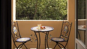 Ein Balkon mit Tisch und zwei Stühlen, ein Fenster mit Blick auf Bäume und ein Fliesenboden.