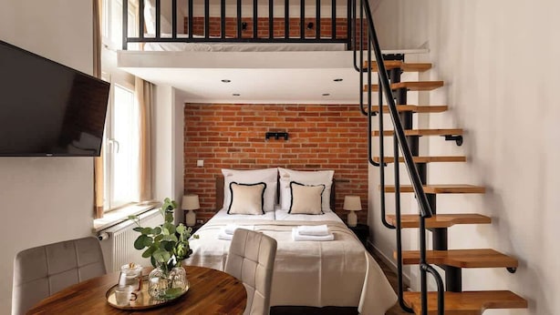 Un dormitorio estilo loft con pared de ladrillo, escalera de madera y zona de comedor con mesa y sillas.