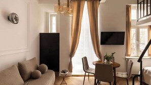 Una sala de estar con sofá, mesa de comedor, sillas, televisor y una escalera.