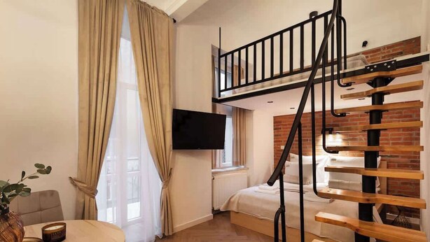 Ein modernes Zimmer mit einer Holztreppe, einem Bett, einem Fernseher und einem Essbereich mit Tisch und Stühlen.