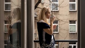 Eine Person steht an einem Fenster mit Blick auf ein Gebäude.