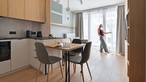 Moderni keittiö, jossa on puiset kaapit, ruokapöytä tuoleineen ja henkilö seisomassa suuren ikkunan vieressä.