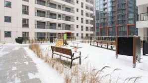 Un edifici de diversos pisos amb balcons, terra coberta de neu i mobiliari exterior.