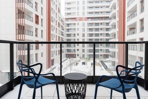 A balcony with two blue chairs and a small round table, overlooking a courtyard with buildings in the background. - Towarowa Square | Balcony & Parking (Warszawa)