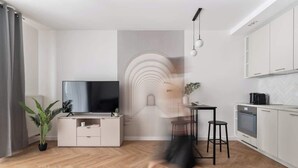 Un saló modern amb televisió de pantalla plana, zona de menjador i cuina amb armaris blancs.