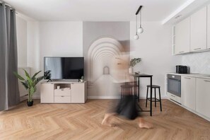 A modern living room with a flat-screen TV, a dining area, and a kitchen with white cabinets. - Towarowa Square | Balcony & Parking (Warszawa)