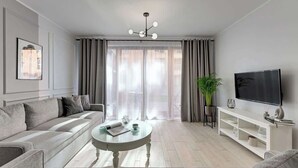Ett modernt vardagsrum med en soffa, ett soffbord, en tv och ett stort fönster med gardiner.